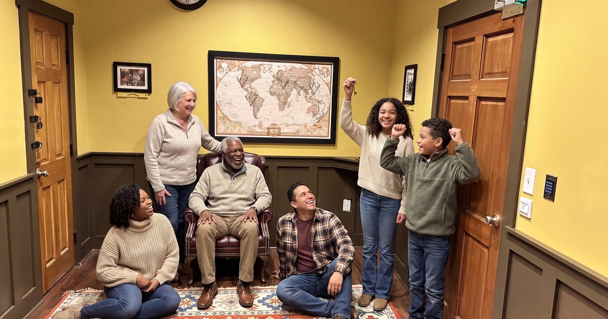 A multigenerational family in cozy sweaters celebrates in The Inheritance escape room study as a teenage girl holds up a brass key and her grandfather laughs in the leather armchair