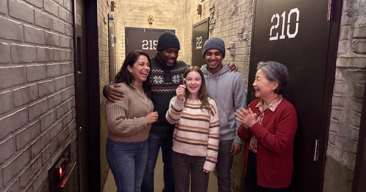 A family home for winter break, including a grandmother in a red cardigan and a college-age son in a hoodie, laughs in the C-Block Prison Break cell-block hallway as the teenage daughter holds up a brass key