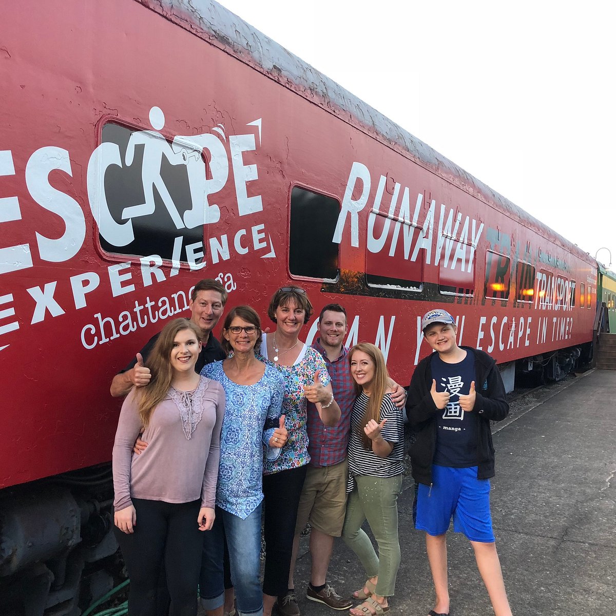 A smiling group gives thumbs up in front of the red Escape Experience Runaway Train car at the Chattanooga Choo Choo